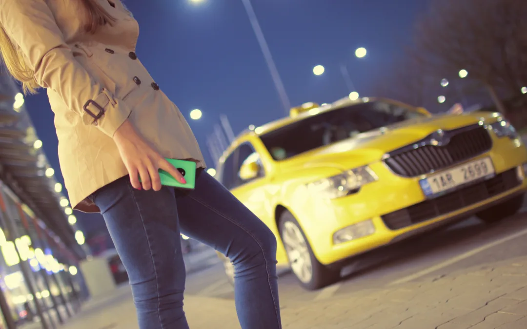 A woman standing on the street with her phone in hand, waiting for a taxi.